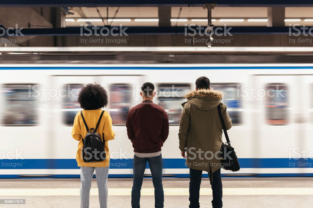 Trein in beweging aan station waar mensen staan te wachten.