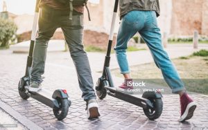 Twee deelscooters met twee mensen in beweging op de stoep