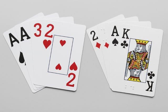 Twee stocks met speelkaarten (grootletterspelkaarten en braillespeelkaarten) op een lichtgrijze ondergrond. De kaarten zijn als een waaier uitgespreid.